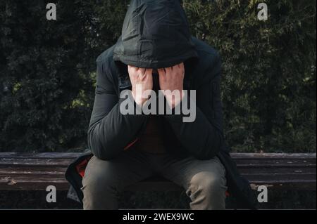 triste homme solitaire sans-abri déprimé et bouleversé assis sur un banc de parc et couvre son visage avec ses mains Banque D'Images