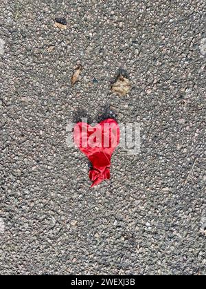 Un ballon en forme de coeur rouge dégonflé gisant forlornly sur un trottoir à londres Royaume-Uni grande-bretagne angleterre angleterre Banque D'Images