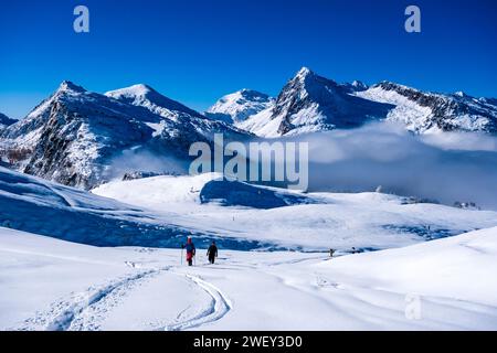 Deux randonneurs en raquettes marchant au-dessus du col Passo Rolle, des sommets de Cavallazza, Cima Val Cigolera et Colbricon Ovest au loin, en hiver. Banque D'Images