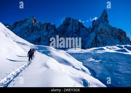 Deux randonneurs en raquettes marchent vers la cabane de montagne Baita Segantini, les sommets du groupe Pale au loin, en hiver. Banque D'Images
