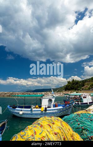 Vieux bateau de pêche traditionnel avec ses filets de pêche jaunes et verts couchés sous le soleil et de grands nuages blancs, dans le nord de la Grèce, Europe. Banque D'Images