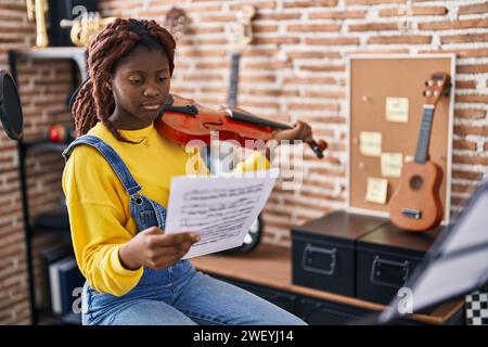 Femme africaine américaine musicienne jouant du violon regardant une feuille de musique dans un studio de musique Banque D'Images
