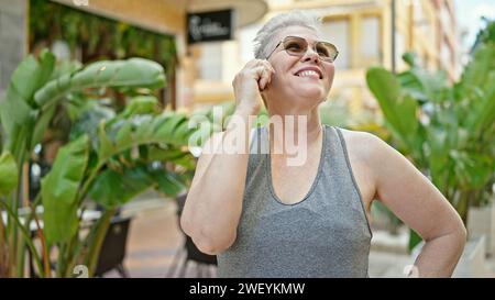 Femme d'âge moyen à cheveux gris souriant confiante parlant sur le smartphone au parc Banque D'Images