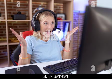 Jeune femme caucasienne jouant à des jeux vidéo portant des écouteurs célébrant fou et étonné de succès avec les bras levés et les yeux ouverts criant excité Banque D'Images