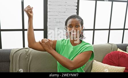 Femme afro-américaine souriant à l'intérieur faisant un exercice d'étirement sur un canapé dans un salon moderne Banque D'Images