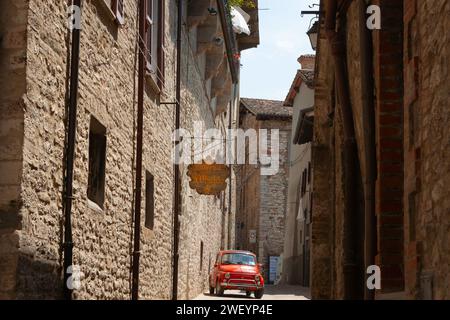 Gubbio Italie - mai 13 2011 ; rue ombragée étroite bordée de grands bâtiments européens avec une petite voiture rouge sous le signe pour la taverne Banque D'Images