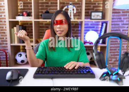 Femme chinoise d'âge moyen portant des lunettes de réalité virtuelle souriant avec le visage heureux regardant et pointant vers le côté avec le pouce vers le haut. Banque D'Images