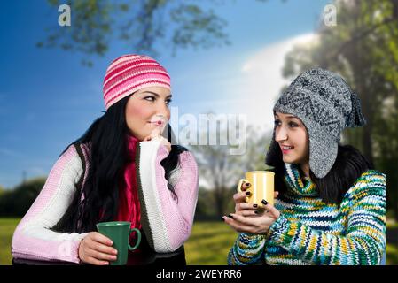 Deux belles jeunes femmes partagent une pause-café joyeuse dans la nature, entourée d’une verdure luxuriante, célébrant amitié et sérénité Banque D'Images