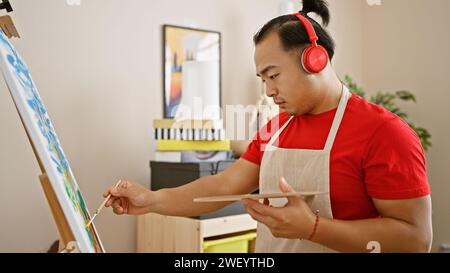 Jeune homme chinois sérieux avec coiffure de queue de cochon, artiste debout dans le studio d'art universitaire, maîtrisant sans effort l'art de dessiner tout en intensément l Banque D'Images