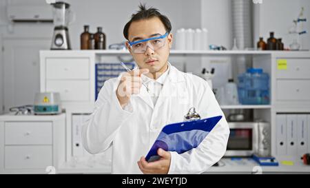 Beau, jeune, homme chinois, scientifique adulte sérieux absorbé dans l'analyse de biologie, méticuleusement prenant des notes sur le presse-papiers tout en parlant passionnément Banque D'Images