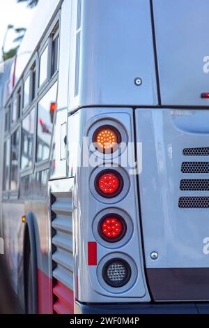 Gros plan des feux stop arrière incandescents d'un autobus urbain se trouvant à un feu de circulation. Feux arrière sur bus blanc. Gros plan, feu arrière d'autobus urbain sur la rue de la ville. Banque D'Images