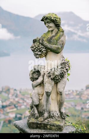 Statue antique de l'ancien dieu grec Dionysos avec une grappe de raisins avec un petit faune avec un bol dans le jardin Banque D'Images
