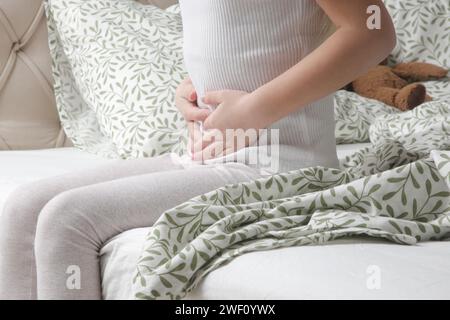 Petite fille couchée sur le lit dans la chambre avec des douleurs à l'estomac. Mains sur le ventre. Banque D'Images