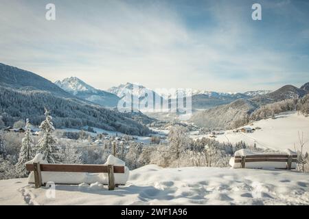 Vue depuis des bancs en bois de grandes montagnes s'élevant au ciel dans la nature enneigée dans les Alpes, ville enneigée se trouve dans la vallée brumeuse encadrée par des forêts de pins Banque D'Images