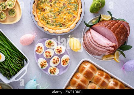 Brunch de Pâques sur une grande table avec jambon tranché en spirale, quiche, œufs diablés et petits pains croisés chauds décorés de Pâques Banque D'Images