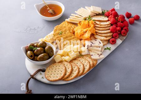 Petit plateau de fromage et de craquelins avec baies fraîches et olives servies avec du miel Banque D'Images