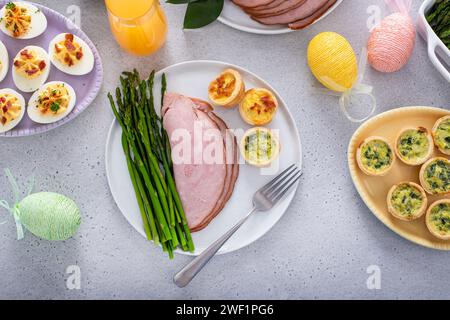 Table brunch de Pâques avec une potion de jambon avec asperges sur l'assiette avec mini quiches Banque D'Images