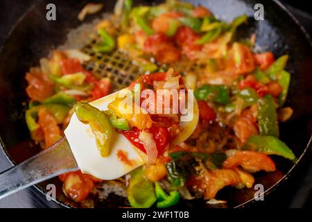 À l'aide d'une poêle en fer, faire sauter les tomates et les poivrons. Banque D'Images