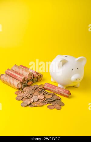 Rouleaux de pièces de monnaie américains avec une tirelire blanche sur un fond jaune Banque D'Images