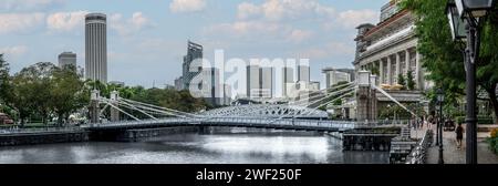 Singapour, le 24 janvier 2024 : le pont Cavenagh s'étend élégamment sur le fleuve Singapour, l'emblématique Fullerton Hotel et d'imposants gratte-ciel. architectural Banque D'Images