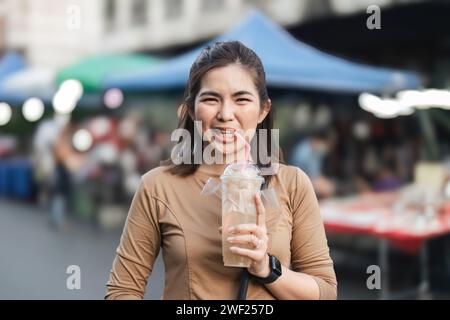 Heureuse jeune femme asiatique voyageur gourmand aiment boire du jus de longan au marché nocturne en plein air vendeur de nourriture de rue Banque D'Images