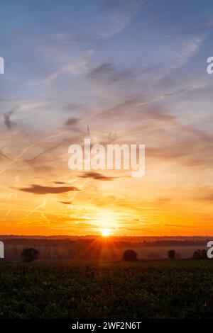 Lever de soleil hivernal sur le petit village de Chislet, Herne Bay dans le Kent. Horizon bas dans le cadre avec des terres agricoles et des champs. Soleil à l'horizon, avec un ciel principalement bleu avec quelques nuages minces dispersés. Banque D'Images