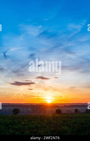 Lever de soleil hivernal sur le petit village de Chislet, Herne Bay dans le Kent. Horizon bas dans le cadre avec des terres agricoles et des champs. Soleil à l'horizon, avec un ciel principalement bleu avec quelques nuages minces dispersés. Banque D'Images