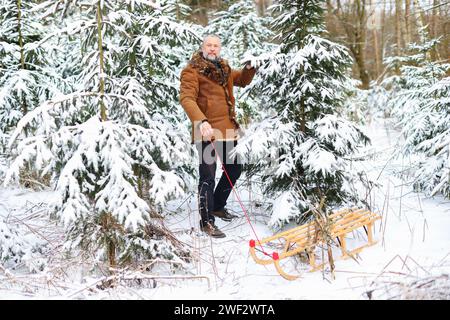 Homme ramassant du bois pour le feu dans la forêt, la nature. gars solitaire dans des vêtements chauds dans la forêt d'hiver enneigée. Banque D'Images