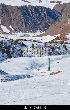 Les gens s'assoient dans des chaises de téléphérique menant au sommet de la piste de ski. Poteau de téléphérique, construction. Activité vacances d'hiver, skieurs, snowboarders, style de vie. Resort Chunkurchak, nature du Kirghizistan. Banque D'Images