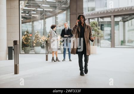 Homme d'affaires de garde marchant devant des collègues dans un hall avec décor de Noël, à l'extérieur. Banque D'Images