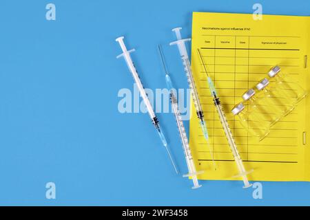 Concept de vaccination avec passeport vaccinal, 4 seringues et flacons sur fond bleu avec espace copie Banque D'Images