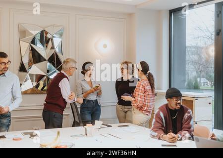 Un groupe de coéquipiers multiraciaux discutent de manière décontractée dans un espace de bureau lumineux et contemporain, en mettant l'accent sur l'interaction et la collaboration. Banque D'Images