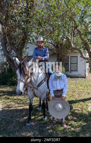 Jeune garçon tenant charro sombrero se tient à côté du cheval avec cow-boy en selle, en attendant le début de Parade of oranges 2024, Mission, Texas, USA. Banque D'Images