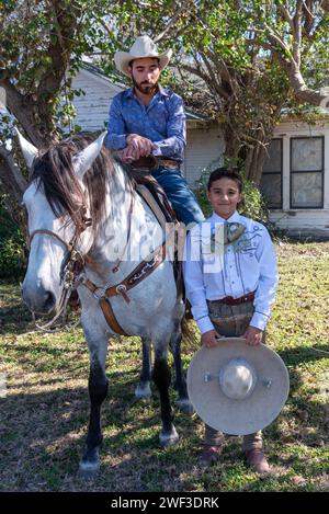 Jeune garçon tenant charro sombrero se tient à côté du cheval avec cow-boy en selle, en attendant le début de Parade of oranges 2024, Mission, Texas, USA. Banque D'Images