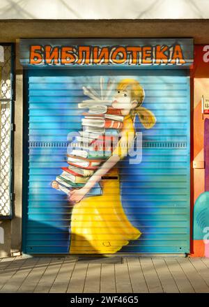 Fille portant une grande pile de livres dans les mains graffiti sur une petite bibliothèque de quartier local porte fermée à Sofia, Bulgarie Banque D'Images