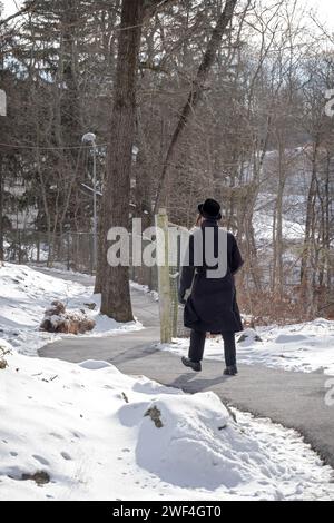 Un juif orthodoxe non identifié vêtu de marche noire sur une route sinueuse à New York pendant l'hiver 2024. Banque D'Images