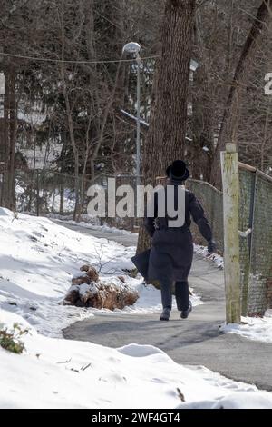 Un juif orthodoxe non identifié vêtu de marche noire sur une route sinueuse à New York pendant l'hiver 2024. Banque D'Images