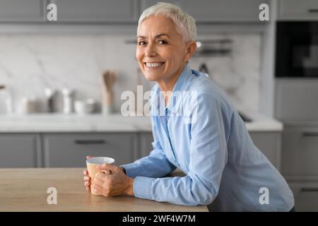 joyeuse femme senior commençant la journée avec tasse de café à l'intérieur Banque D'Images