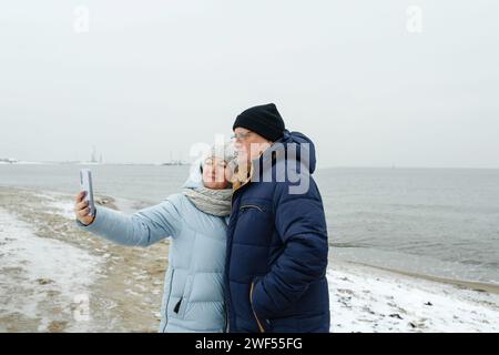 Portrait d'un couple de personnes âgées profitant d'une promenade hivernale sur la plage, prenant un selfie. Banque D'Images