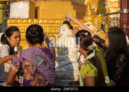 Groupe de femmes locales versant de l'eau sur une statue de Bouddha à la pagode Shwedagon à Yangon, Myanmar, un matin ensoleillé. Banque D'Images