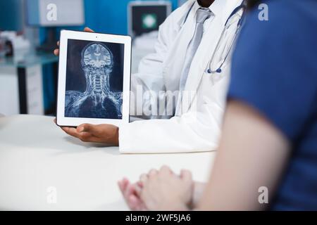 Gros plan des résultats radiographiques sur tablette électronique dans un cabinet médical. Le médecin noir tient le dispositif avec la radiographie du cerveau et des os, montrant la présence de tumeurs ou de maladies et symptômes graves. Banque D'Images