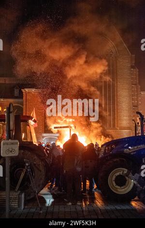 Turnhout, Anvers, Belgique, 28 janvier 2024, cette image puissante capture un moment de protestation sous le ciel nocturne à Turnhout, en Belgique, où les agriculteurs se sont réunis pour exprimer leur désaccord contre l'accord sur l'azote. Les braises brûlantes et la fumée dense qui s'élèvent dans l'air créent une toile de fond spectaculaire pour les tracteurs aux lumières bleues flanquant la scène. Les manifestants, visibles seulement en silhouette, sont rassemblés autour du feu, les flammes reflétant leur détermination et la gravité de leur cause. L’ambiance est intense et chargée, reflétant les conversations cruciales autour de l’agricult Banque D'Images