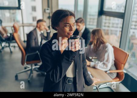 Femme d'affaires avec café debout dans la salle de réunion sur le fond des collègues et regarde loin Banque D'Images