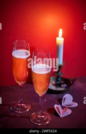 deux verres de champagne et une bougie allumée sur fond rouge Banque D'Images