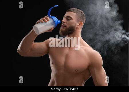 Jeune homme avec le corps musculaire buvant des protéines shake sur fond noir Banque D'Images