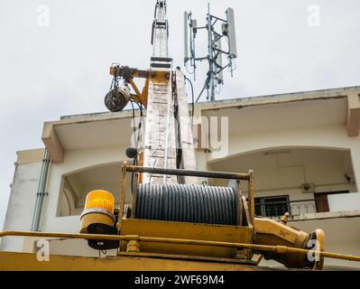 Grue industrielle exploitant la tour de télécommunications sur le bâtiment contre les nuages et le ciel Banque D'Images