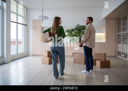 Famille heureuse emménager dans un nouvel appartement propre, portant des boîtes en carton avec des effets personnels, des plantes en pot Banque D'Images