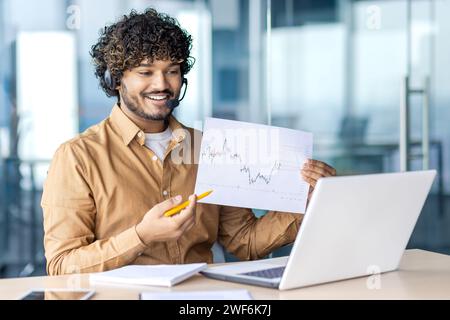 Employeur hispanique optimiste dans les écouteurs sans fil menant la vidéoconférence et montrant le graphique statistique avec des résultats impressionnants. Responsable du département marketing partageant les résultats d'une stratégie réussie. Banque D'Images