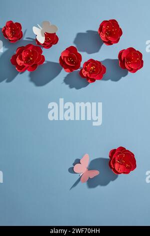 Vue de dessus de fleurs de papier rouge, papillons blancs et roses sur fond bleu. Flan pour carte publicitaire ou invitation. Concept de fleur printanière. Plat Banque D'Images