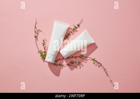 Scène de nature minimaliste abstraite - bouteilles vides et petites fleurs sur fond pastel corail rose tendance. Maquette pour le design, cosmétiques biologiques, beauté p Banque D'Images